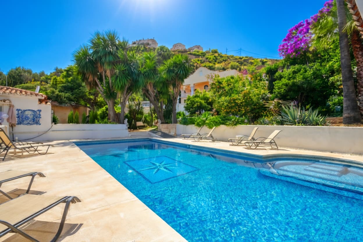 Piscina azul rodeada de tumbonas, palmeras y vegetación exuberante bajo un cielo despejado y soleado.