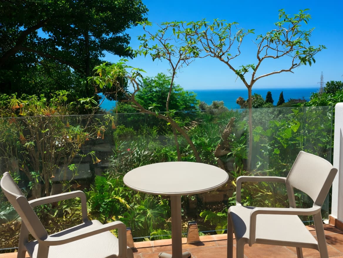 Terraza soleada con muebles modernos, vegetación frondosa y vistas panorámicas al mar azul profundo.