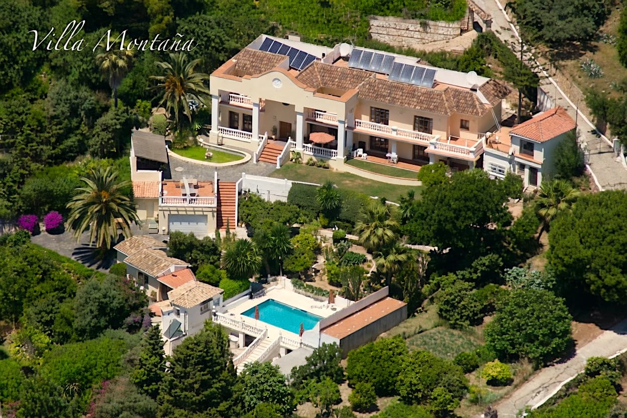 Vista aérea de Villa Montaña con paneles solares, piscina y jardines rodeados de palmeras.